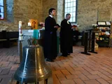 Geistliche im Talar neben einer Glocke in der Kirche