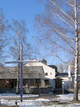Die Auferstehungskirche in Puchheim im Winter, davor ein Kreuz und Birken